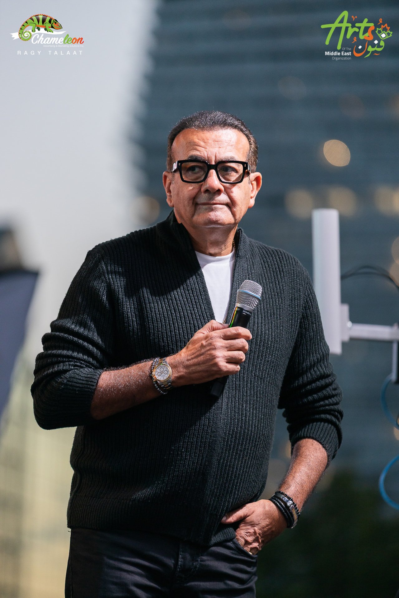 Osama Mounier on stage holding a mic with city towers behind
