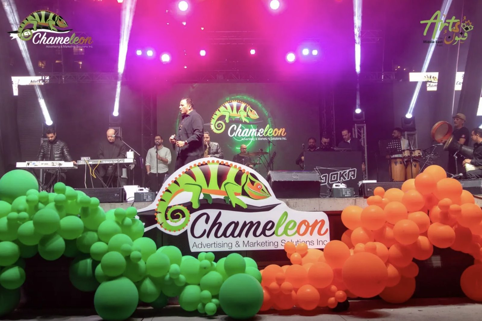 Singer and band performing on a brightly lit festival stage with green and orange balloon arches